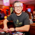 Mario Manni mit Kopfhörern auf an der Mixing-Console schaut lächelnd in die Kamera