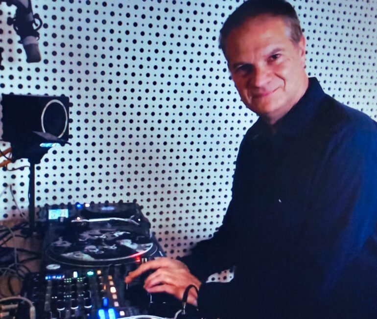 Funky Stevie schaut in die Kamera während er vor einem DJ Mixing Deck steht in einem Radiostudio steht.