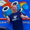 Hajo steht vor einem ANhönger mit Shake!FM T-Shirt, lächelt und streckt beide Daumen nach oben