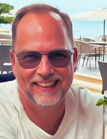 Lutz WOllgarten im Porträt mit Cocktail in der Hand lächelt er in die Kamera aus einem Hotel