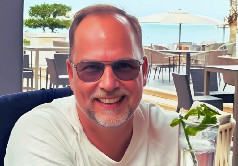 Lutz WOllgarten im Porträt mit Cocktail in der Hand lächelt er in die Kamera aus einem Hotel