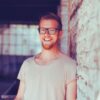 Markus Steinacker schaut im Porträt lächelnd direkt in die Kamera und steht dabei angelehnt an einer Mauer.