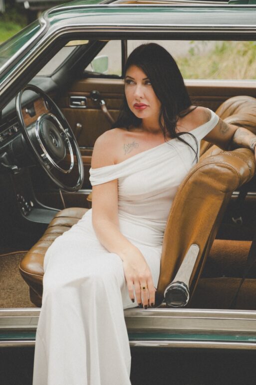Sängerin Myriam-Catharina mit weissem Kleid in einem alten Mercedes-Benz auf dem Fahrersitz