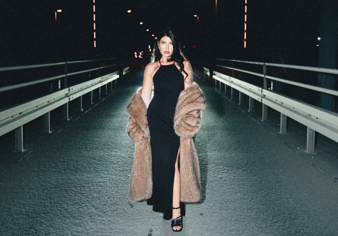 Sängerin Myriam-Catharina mit Kleid und Mantel nachts auf einer Brücke
