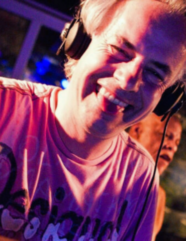 Bernd Niedergesäß in seinem Element als DJ, mit Kopfhörern auf und lacht in die Kamera